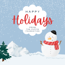 text: Happy Holidays from The Puffin Foundation Image: a blue sky with snow falling on a snowman with a pine tree nearby